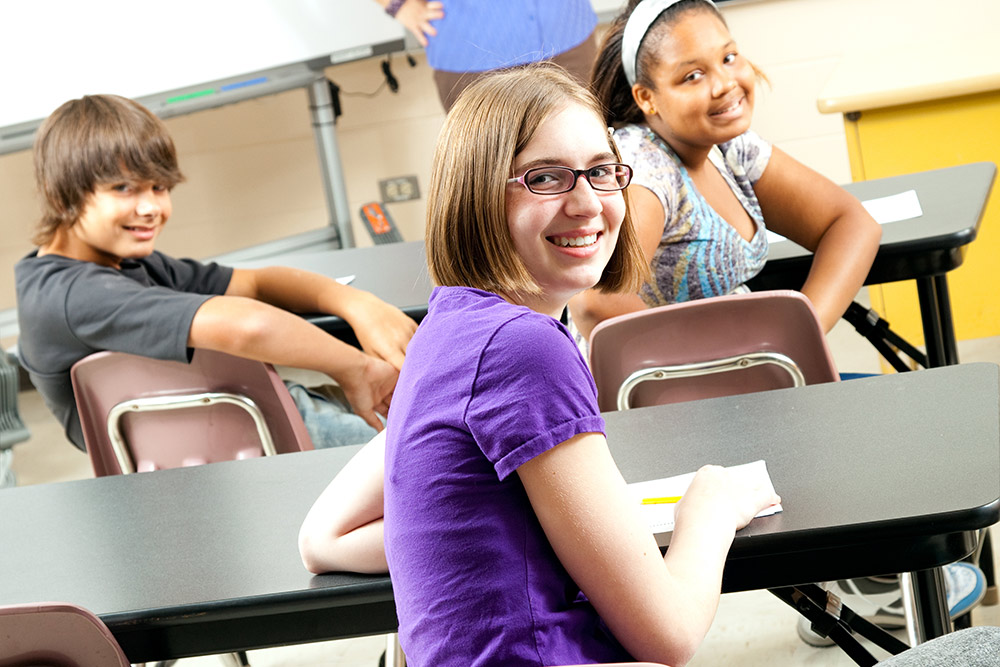 High school age kids sitting at tables in a classroom.