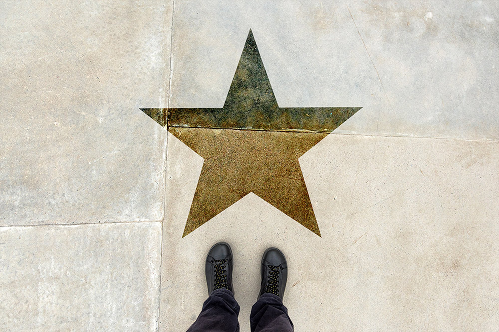 Looking down at gold star painted on the ground and two feet visible standing next to it.